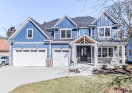 White short raised panel garage doors with arched window lites on a blue two-story home