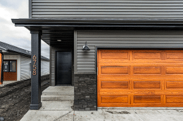 Cedar woodtone raised panel garage door on a modern gray home with stone accents